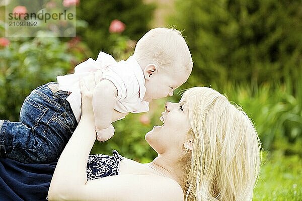 Glückliche junge Frau spielt mit Baby Junge im Frühling blühenden Garten. Natur unscharfen Hintergrund