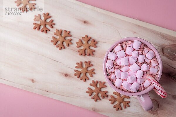 Winterliche Süßigkeiten in Rosatönen  eine Tasse heiße Schokolade mit Mini Marshmallows und einer weihnachtlichen Zuckerstange sowie Lebkuchen in Form von Schneeflocken