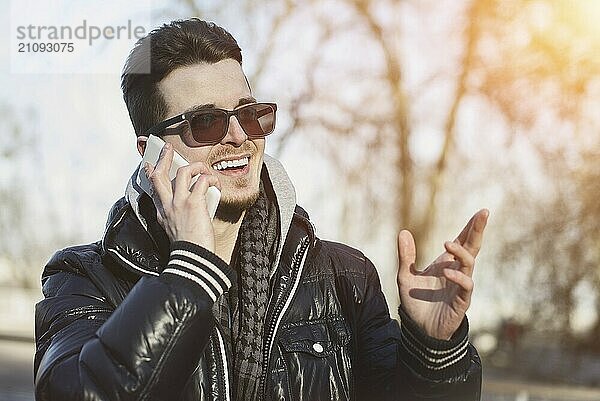 Ein Mann in einer warmen Jacke mit einem Smartphone in der Hand  ein sonniger Tag