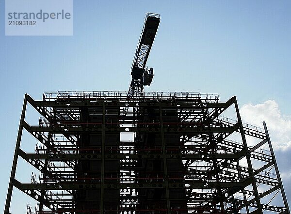 Eine große Baustelle in Silhouette am Abend mit Stahlträgern und einem Kran in Silhouette gegen einen blauen bewölkten Himmel