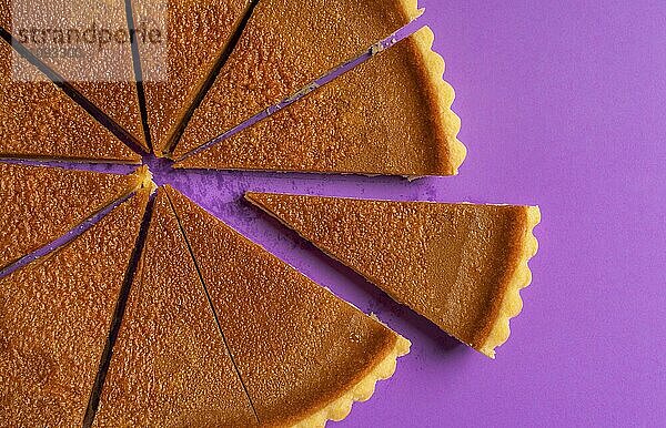 Draufsicht auf einen aufgeschnittenen Kürbiskuchen mit einem abgetrennten Stück. Traditionelles Thanksgiving Dessert. Hausgemachter Herbstkuchen. Minimalistischer Stil. Lila Hintergrund