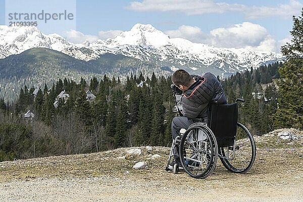 Foto eines Mannes im Rollstuhl mit Kamera in der Natur  der schöne Berge fotografiert