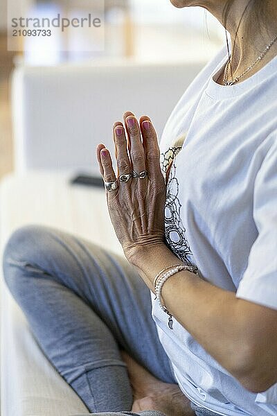 Close-up of the hands of a mid-adult woman meditating on her sofa at home  with natural daylight and hands in Anjali Mudra at heart center