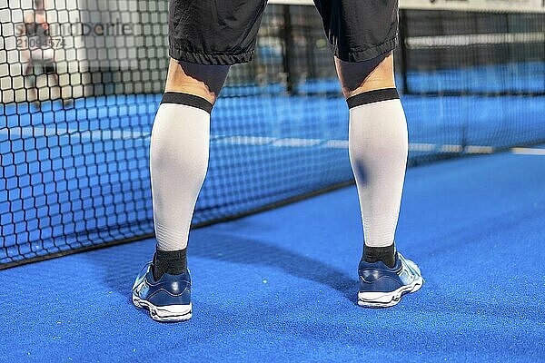 Beine eines sportlichen Mannes  der mit Freunden auf einem blauen Hallenplatz Paddle Tennis spielt