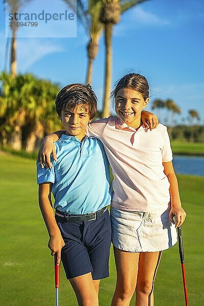 Vertikales Porträt einer kaukasischen jungen Schwester und eines Bruders  die sich in einem grünen Golfplatz umarmen und lächeln