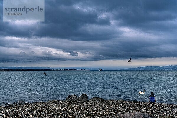 Landschaft mit dem Bodensee in der Stadt Friedrichshafen  Deutschland  an einem regnerischen Tag  während ein Mann am Ufer sitzt und meditiert  Europa