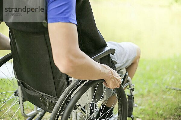 Junger behinderter Mann in einem Rollstuhl sitzend in der Natur  der die Räder dreht und hält