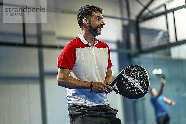 Älterer sportlicher Mann spielt Paddle Tennis mit Freunden in einer Halle