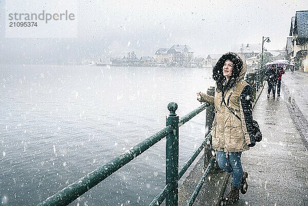 Winter Freude Thema Bild mit einer jungen Frau lachend und genießen den Schneefall  auf dem Hallstatter See Ufer  in der berühmten Hallstatt Stadt  in Österreich