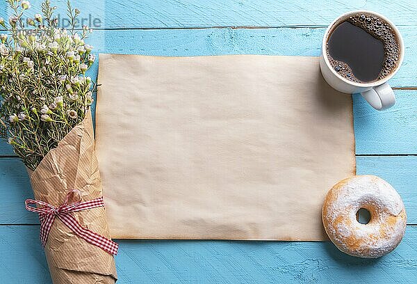 Frühlingsblumenstrauß  leerer alter Papierbogen  heißer Kaffee und ein Donut auf blauem Hintergrund. Romantisches Frühstücks Setup. Frühling Kontext. Frauentag. Ansicht von oben