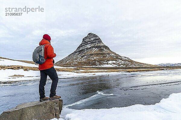 Ein Mann mit dem Rücken zur Landschaft des Berges Kirkjufell im Winter in Island