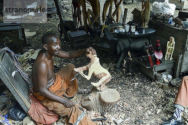 Kenianischer Bildhauer  der den Umriss einer hölzernen Löwin in einer Genossenschaft in Mombasa zeigt