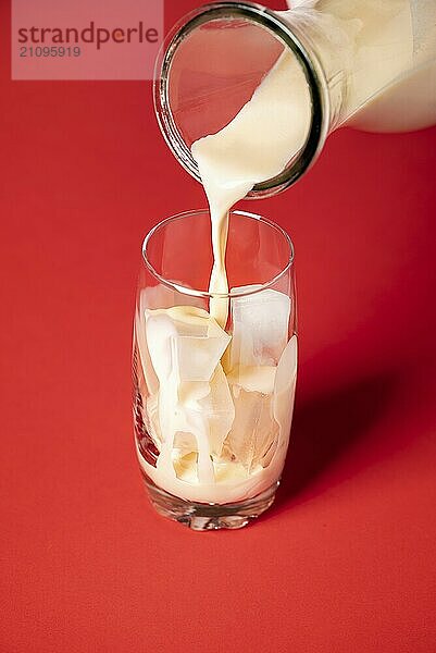 Herstellung von Horchata Mocktail Kontext. Horchata Milch in ein Glas mit Eiswürfeln auf rotem Hintergrund gießen Servieren eines mexikanischen Sommergetränks. Hausgemachtes Getränk