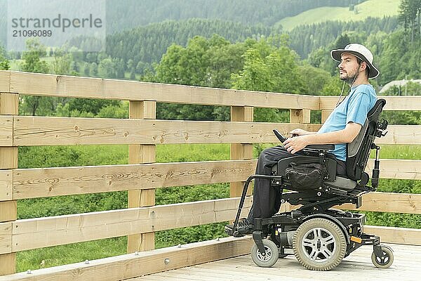 Photo of disabled Young man in electric wheelchair on a boardwalk enjoying his freedom and observing nature