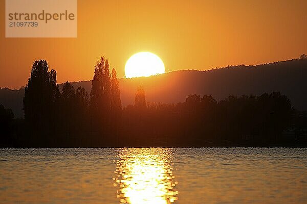 Sonnenuntergang über einem See mit spiegelndem Wasser  Silhouetten von Bäumen im Hintergrund die Insel Reichenau  Bodensee  Baden-Württemberg  Deutschland  Europa