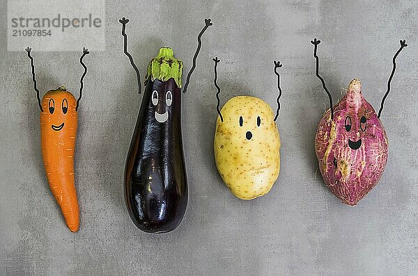 Großes Konzept der gesunden Ernährung  Gemüse mit glücklichen Gesichtern mit Armen nach oben  Kartoffel  Süßkartoffel  Karotte  Aubergine. Grauer Hintergrund  polierter Beton