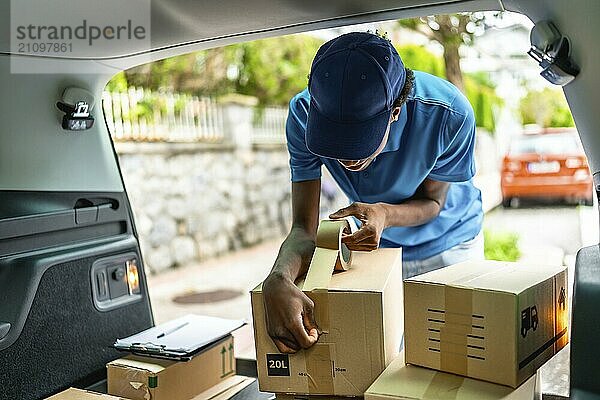 Lieferung afrikanischer junger Mann  der ein Kartonpaket mit Klebeband im Lieferwagen versiegelt