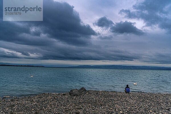 Der Bodensee von Friedrichshafen  Deutschland  aus gesehen  unter stürmischen Wolken und einem Mann  der am Ufer sitzt und denkt  Europa