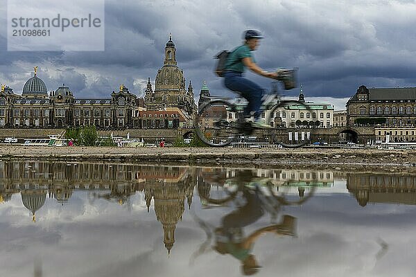 Die Dresdner Silhouette mit einem Radfahrer und dunklen Wolken hinter der Frauenkirche  spiegelt sich am Elberadweg in einer Pfütze.  Elberadweg  Dresden  Sachsen  Deutschland  Europa