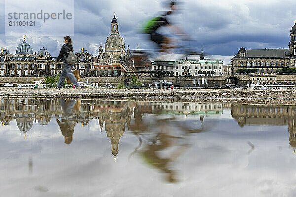 Die Dresdner Silhouette mit einem Radfahrer und dunklen Wolken hinter der Frauenkirche  spiegelt sich am Elberadweg in einer Pfütze.  Elberadweg  Dresden  Sachsen  Deutschland  Europa