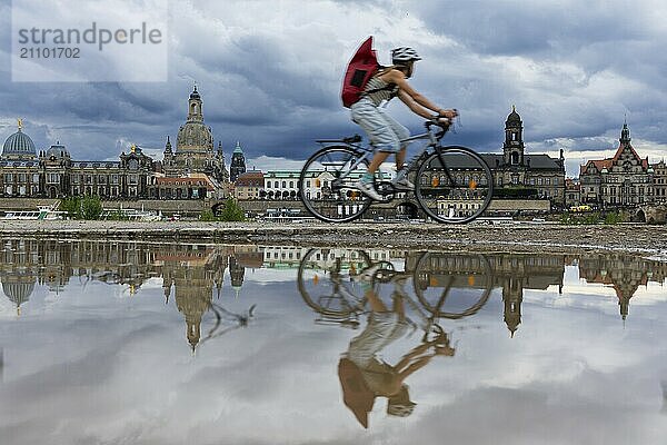 Die Dresdner Silhouette mit einem Radfahrer und dunklen Wolken hinter der Frauenkirche  spiegelt sich am Elberadweg in einer Pfütze.  Elberadweg  Dresden  Sachsen  Deutschland  Europa