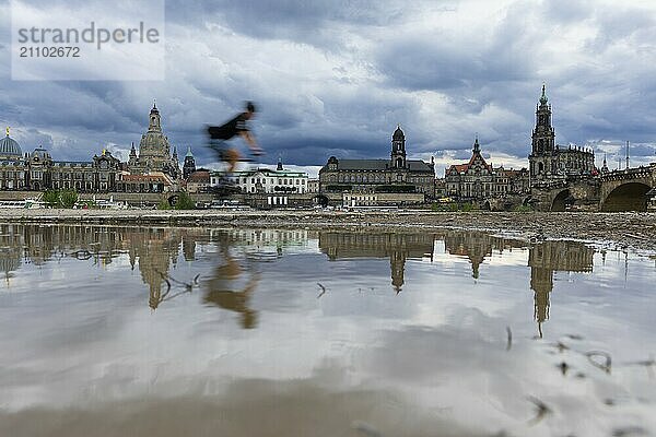 Die Dresdner Silhouette mit einem Radfahrer und dunklen Wolken hinter der Frauenkirche  spiegelt sich am Elberadweg in einer Pfütze.  Elberadweg  Dresden  Sachsen  Deutschland  Europa