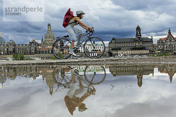 Die Dresdner Silhouette mit einem Radfahrer und dunklen Wolken hinter der Frauenkirche  spiegelt sich am Elberadweg in einer Pfütze.  Elberadweg  Dresden  Sachsen  Deutschland  Europa