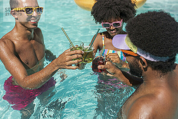 Happy friends together toasting with drinks in pool on sunny day