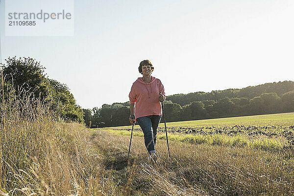 Senior woman holding hiking poles and walking on meadow