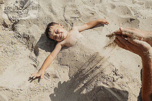 Hand of father covering son with sand