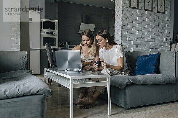 Woman using laptop and sitting with friend at home