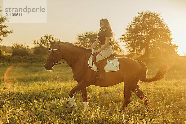 Girl doing horseback riding in meadow on sunny day