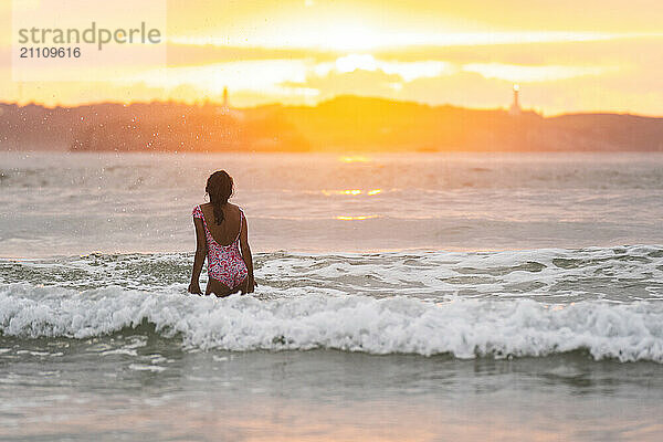 Girl standing in water and looking at view during sunset