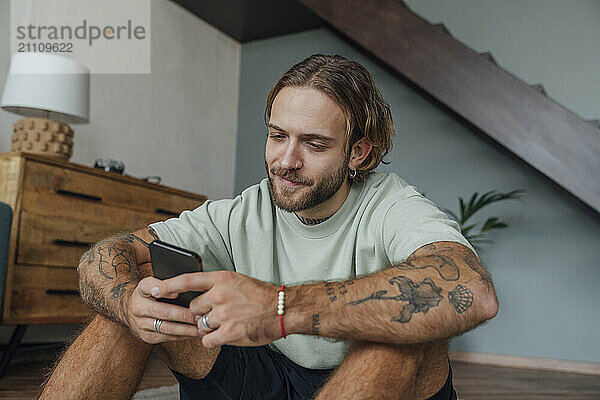 Smiling young man using smart phone at home