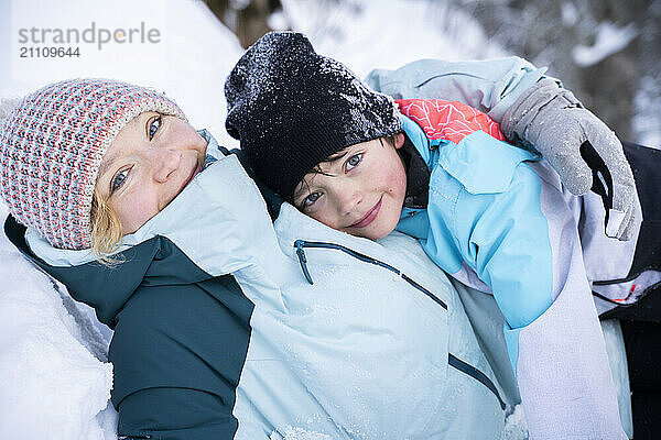 Smiling mother and son in warm clothing lying on snow at winter