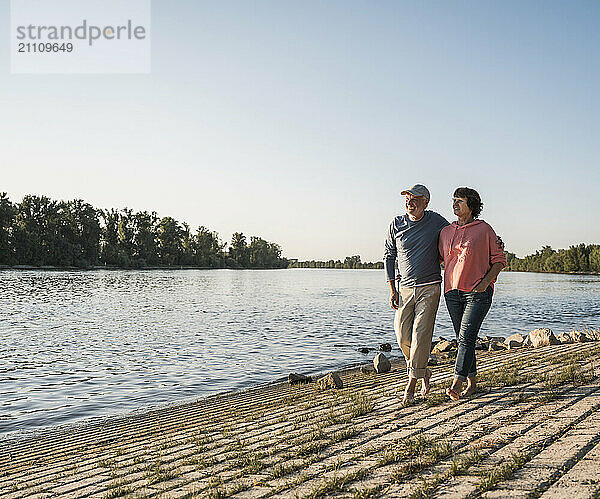 Senior couple walking together at riverbank on sunny day