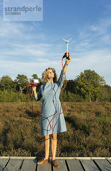 Girl generating electricity with small wind turbine near agricultural field