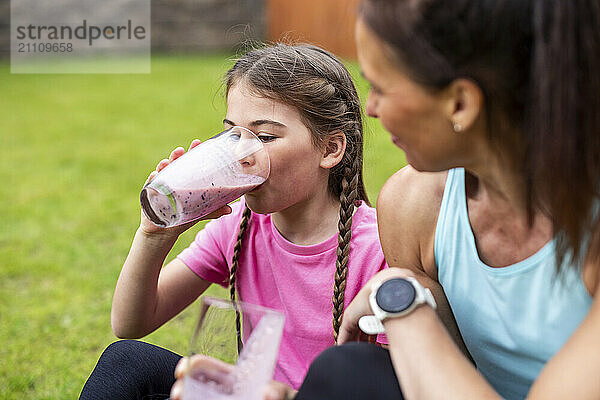 Girl drinking fresh smoothie with mother in back yard