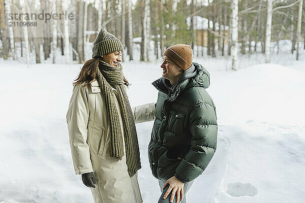 Smiling woman talking with man standing on snow in winter