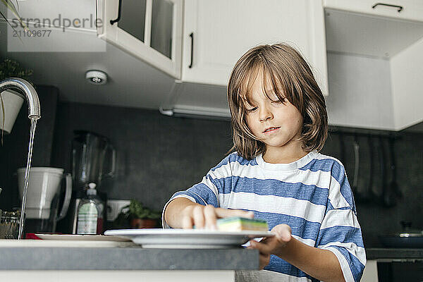 Boy washing dishes near sink in kitchen