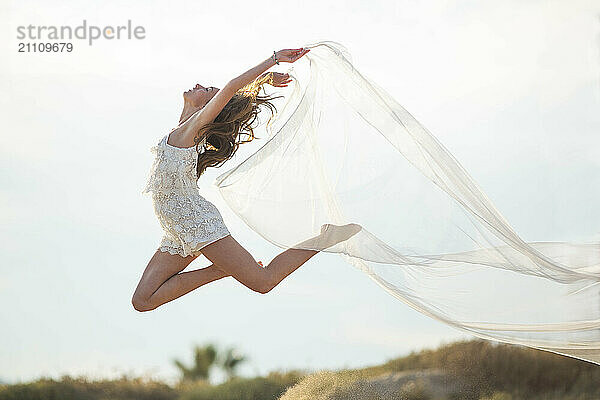 Young woman holding cloth and dancing in mid air at beach