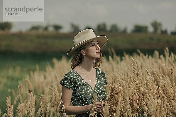 Beautiful woman with hat standing amidst reeds on sunny day