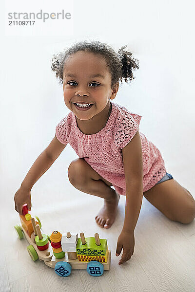 Happy girl with toy vehicle kneeling on floor at home