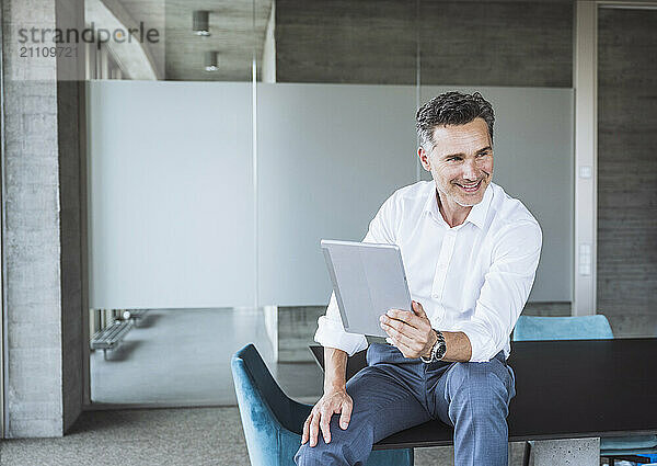 Smiling businessman sitting with tablet PC on desk