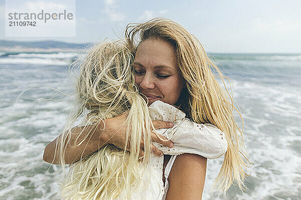 Smiling mother hugging daughter at beach