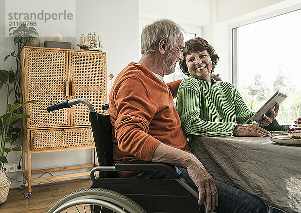 Cheerful senior couple sitting near table and using digital tablet at home