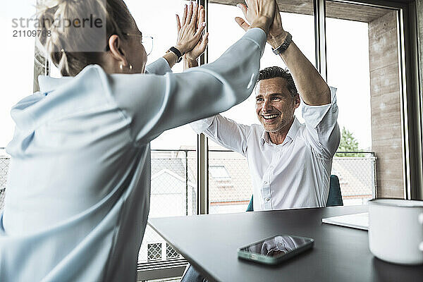 Smiling mature businessman giving high-five to colleague at desk in office