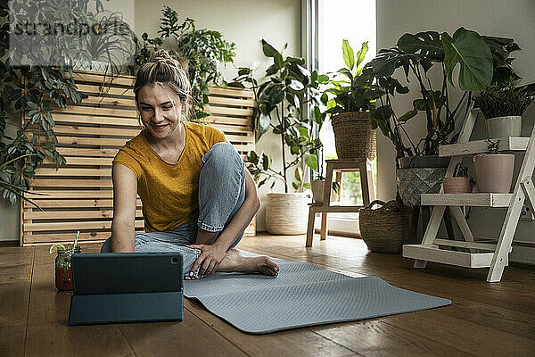 Smiling woman using tablet PC sitting on exercise mat at home