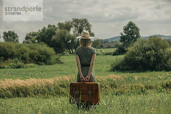 Woman in green dress with suitcase standing near reeds