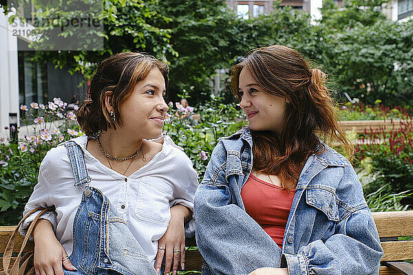 Young gay couple sitting on bench and looking at each other in public park